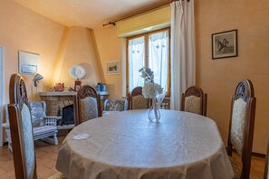 Comedor con una mesa redonda, sillas, un jarrón, chimenea y una ventana con cortinas.