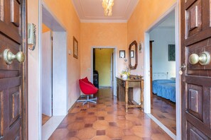 Un pasillo con una silla roja, puertas de madera, una mesita y una cama al fondo.