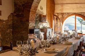 A dining table set with glassware, candles, and plates, in a room with stone walls and arched windows.