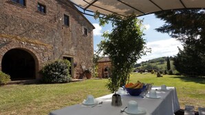 An outdoor dining area with a table set for a meal, a stone building in the background, and a grassy landscape. - Villa 'La Memoria Del Tempo' with Private Pool, Wi-Fi and Air Conditioning (Montalcino)