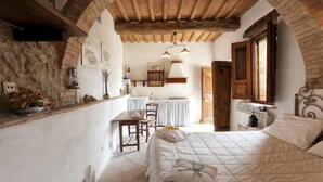 A bedroom with a stone wall, wooden ceiling beams, a bed with a quilt, a bedside table, and a window. - Villa 'La Memoria Del Tempo' with Private Pool, Wi-Fi and Air Conditioning (Montalcino)