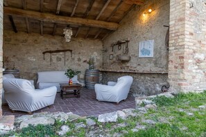 A rustic outdoor seating area with stone walls, a brick floor, and a wooden ceiling.