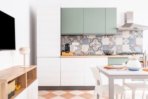 A modern kitchen with white cabinets, a tiled backsplash, and a dining area with a table and chairs. - Apartment 'Corte Curatolo - Ciuri' with Shared Terrace, Wi-Fi and Air Conditioning (Martano)