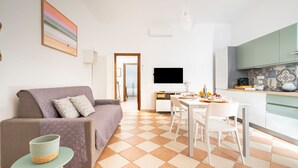 Una sala de estar moderna con sofá, una mesa de comedor y una zona de cocina con televisor.