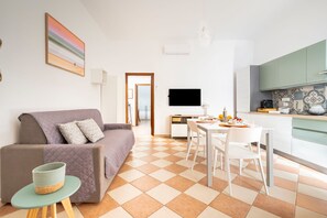 Un salon moderne comprenant un canapé, une table à manger et un coin cuisine avec un téléviseur.
