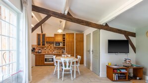 Una cocina con armarios de madera, una mesa de comedor con sillas, un televisor en la pared y una estantería.