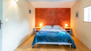 Un dormitorio con cama, dos mesitas de noche, una lámpara de pared y un ventanal con persianas.