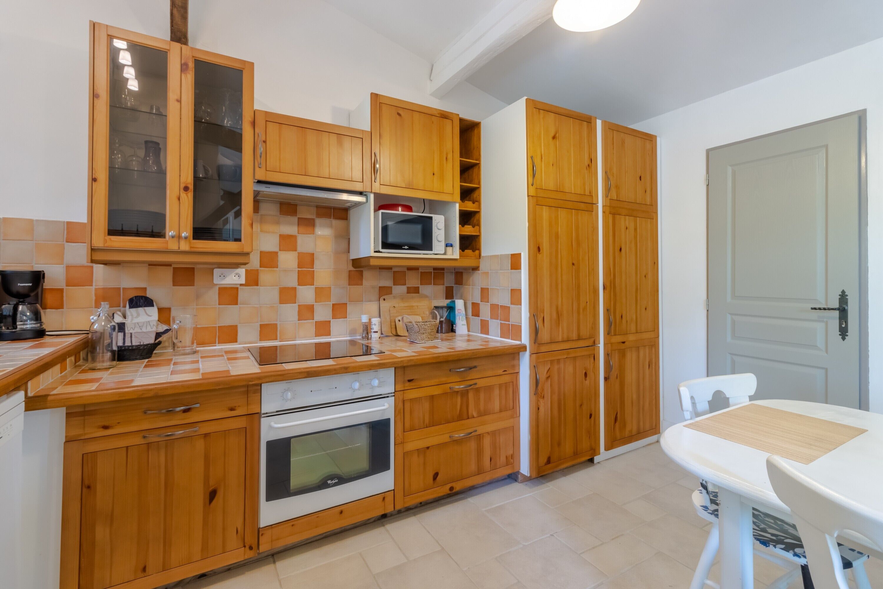 Een keuken met houten kastjes, een magnetron, een oven en een eettafel.