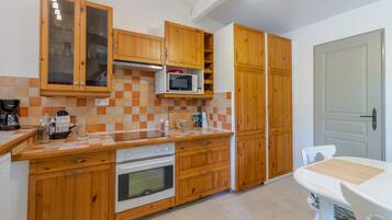 Een keuken met houten kastjes, een magnetron, een oven en een eettafel.