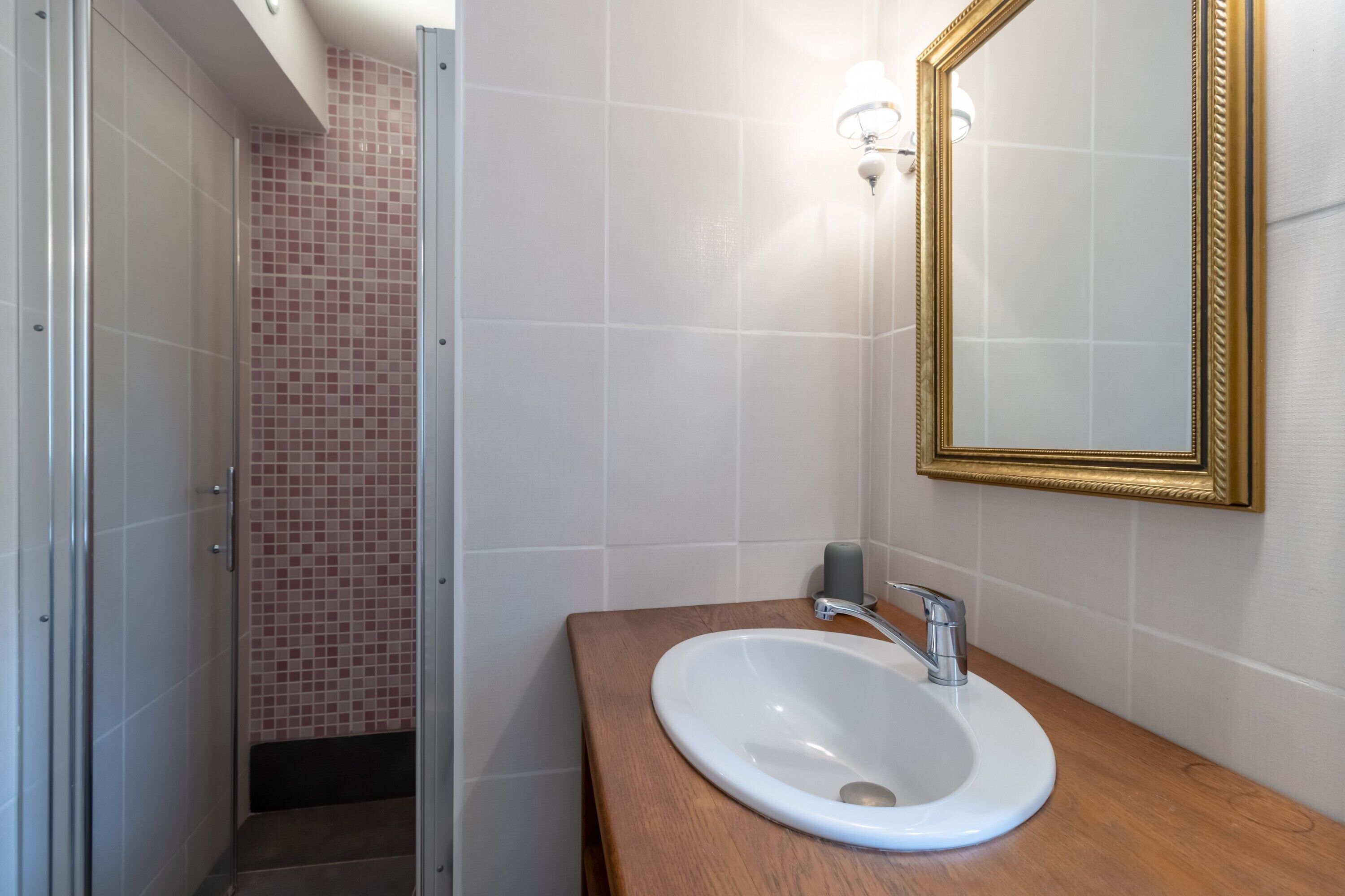 A bathroom with a white sink, a gold-framed mirror, and a shower with pink tiles.