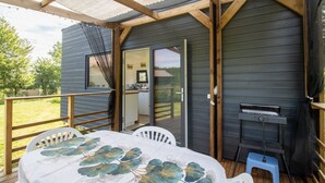 A wooden deck with a table and chairs, a grill, and a sliding door to a kitchen area. - Tiny House in Saint-Cernin-de-l'Herm – Shared Pool & Relaxing Stay for 4 Guests (SAINT-CERNIN-DE-L'HERM)