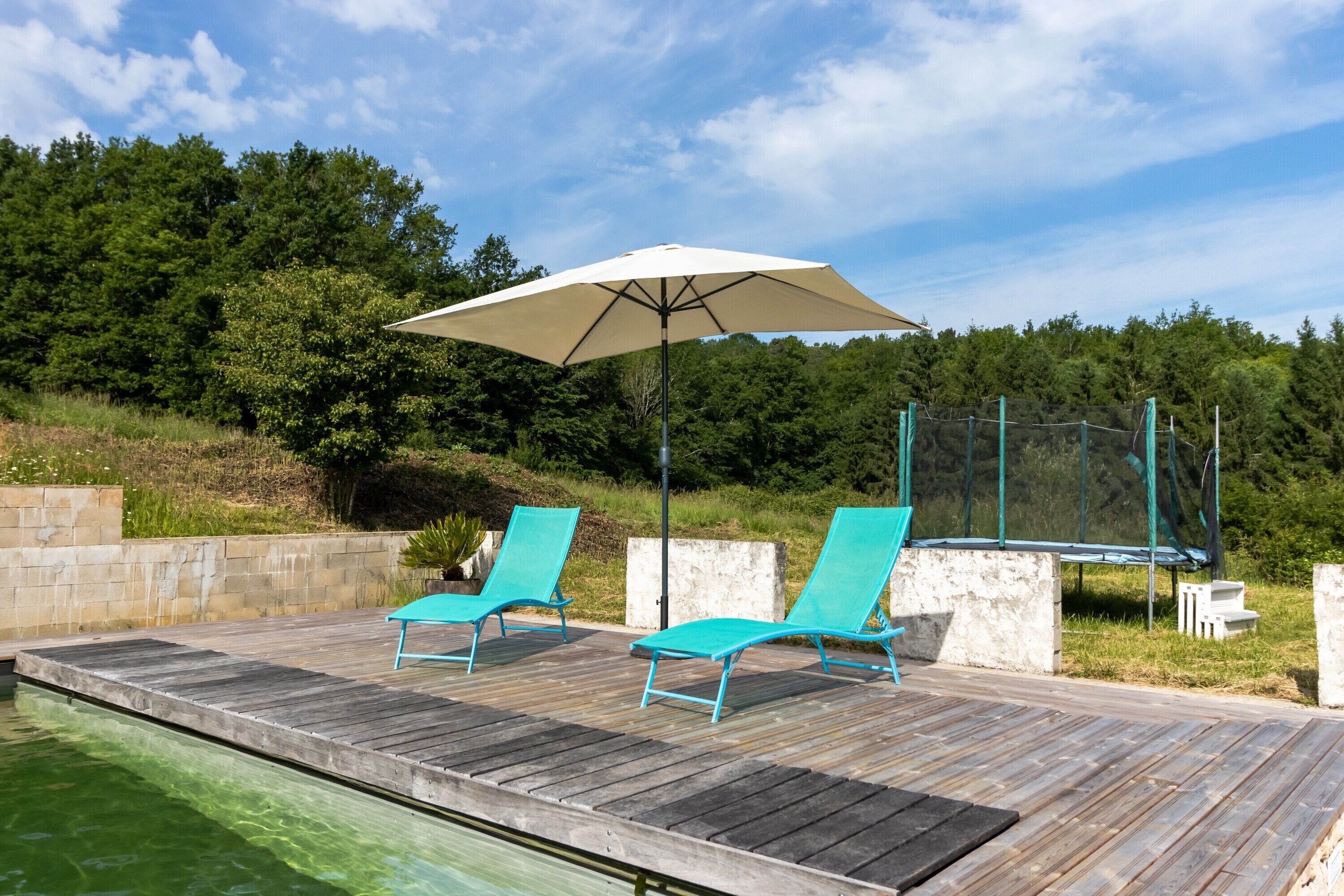 Une terrasse en bois avec deux chaises longues turquoise et un grand parasol.