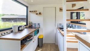 A compact kitchen with a window, built-in microwave, and a trash bin. - Tiny House in Saint-Cernin-de-l'Herm – Shared Pool & Relaxing Stay for 4 Guests (SAINT-CERNIN-DE-L'HERM)