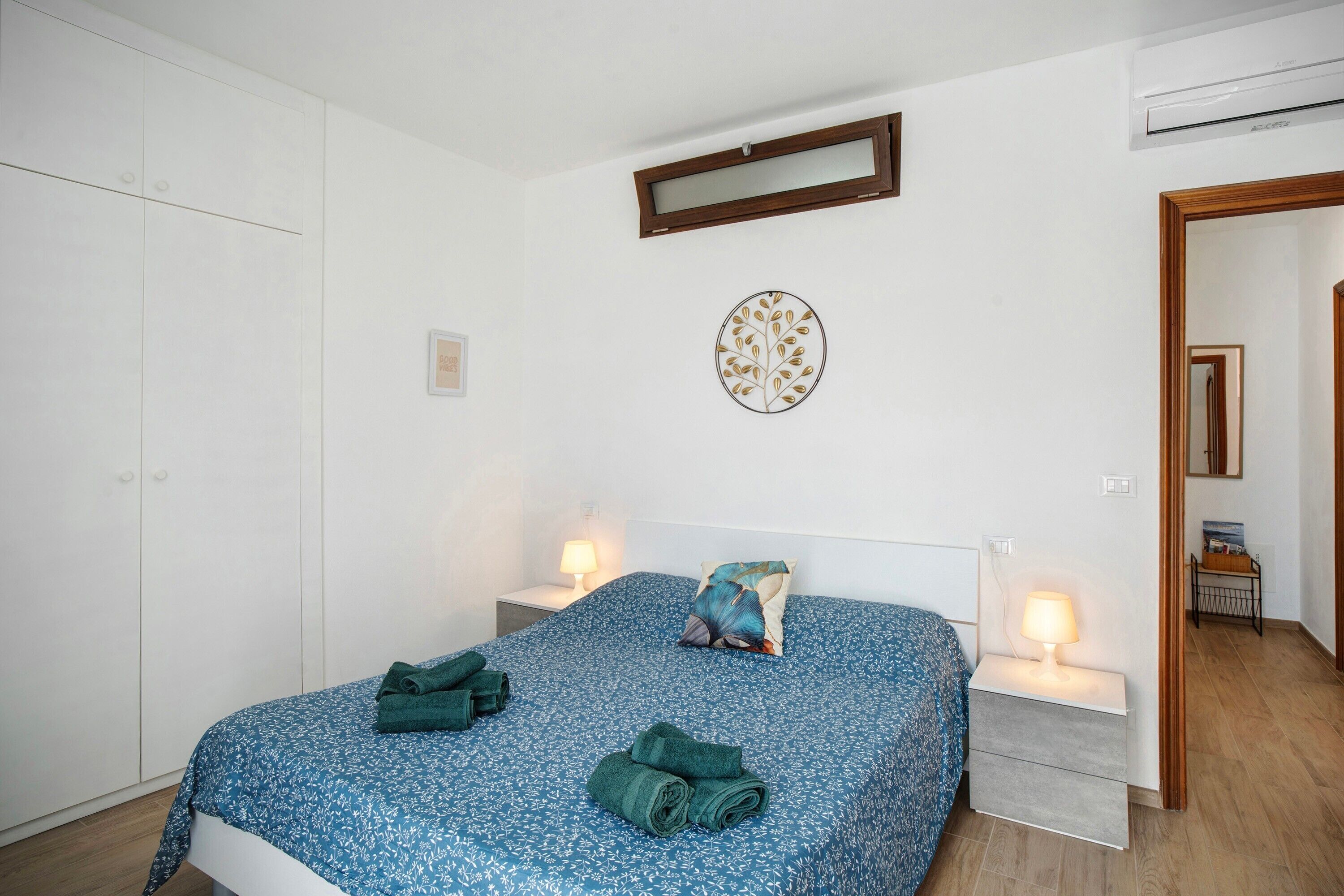 Een slaapkamer met een bed, twee nachtkastjes, een wandspiegel en een kledingkast.