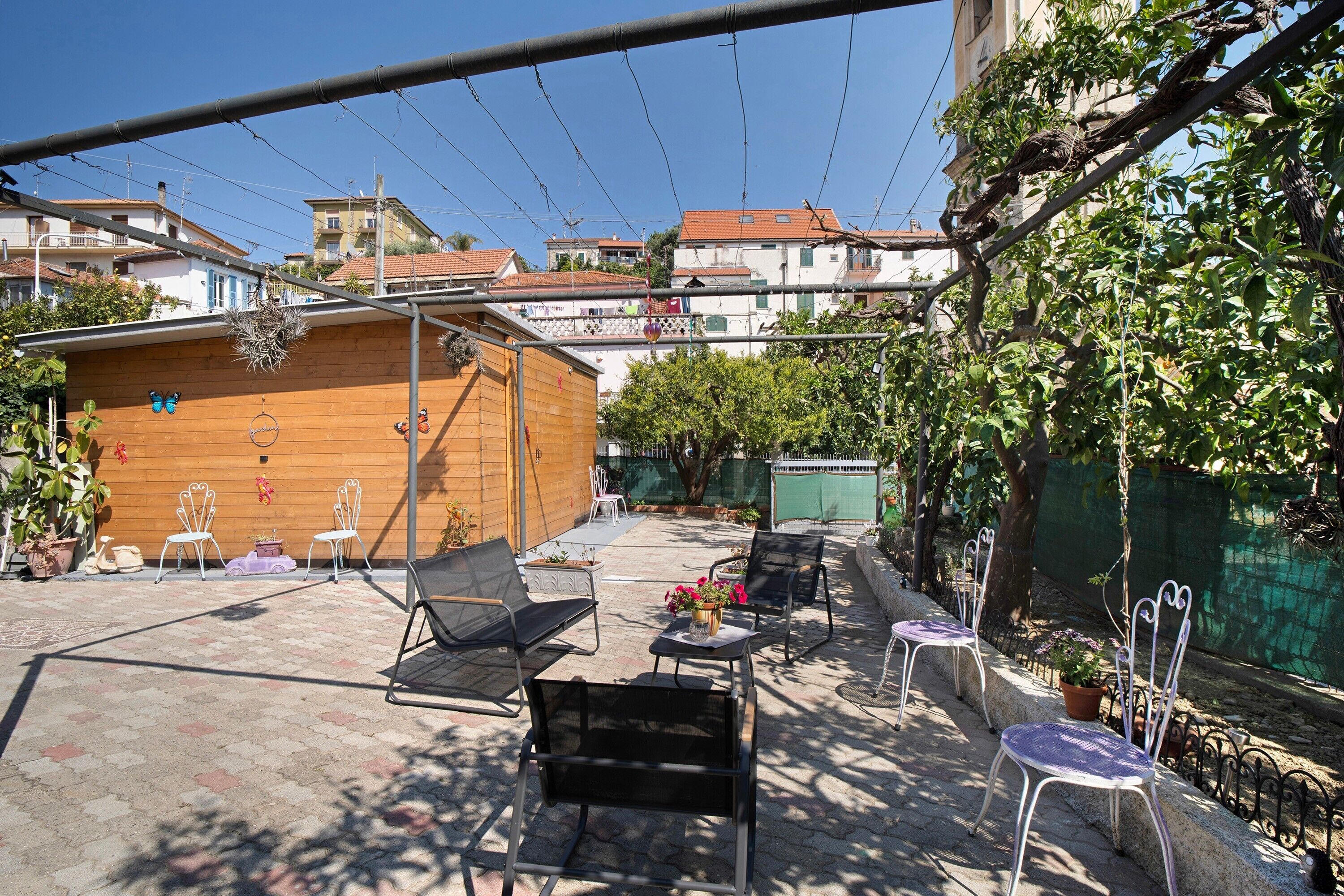 An outdoor patio area with metal chairs, a wooden table, and potted plants.