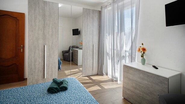 Ein Schlafzimmer mit Bett, Kommode, Fernseher und Blick ins Freie.