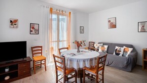 Ein Wohnzimmer mit Esstisch, Stühlen, einer Couch, einem Fernseher und Kunstwerken an den Wänden.