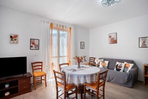 A living room with a dining table, chairs, a sofa, a TV, and artwork on the walls.