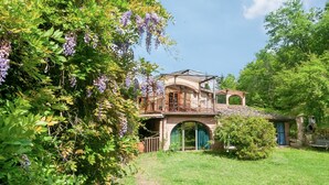 Una casa rústica con un arco de piedra, un balcón de madera y abundante vegetación.