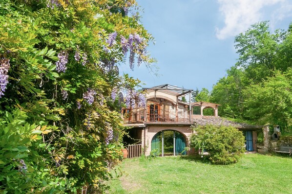A rustic house with a stone archway, a wooden balcony, and lush greenery.