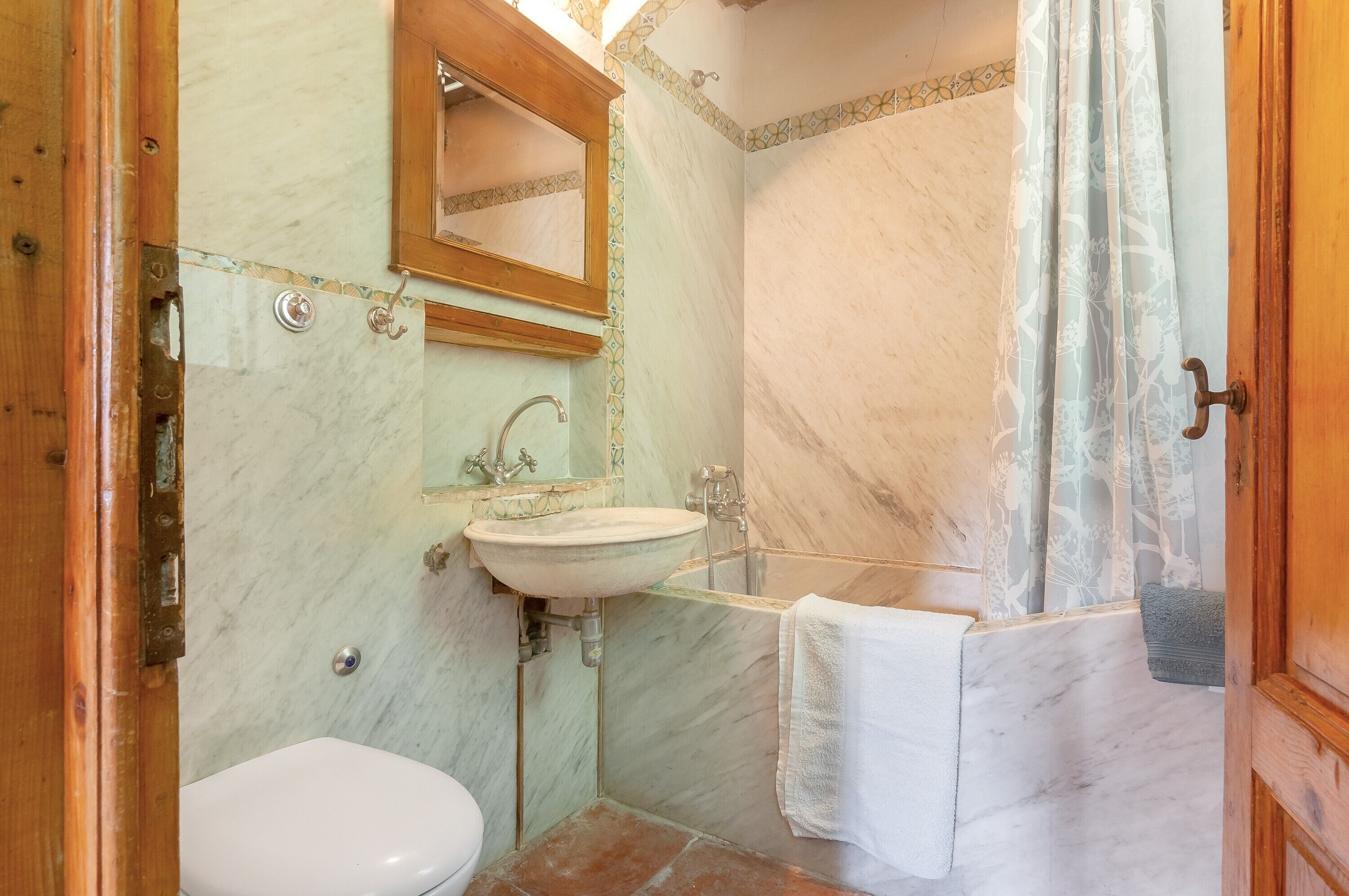 Une salle de bain avec un lavabo en marbre, des toilettes, une douche avec un rideau et une porte en bois.