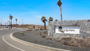 A stone wall with a sign reading 'OrigoMare' and palm trees in a desert landscape. - Vacation 'Punta Calma' with Sea View, Shared Pool and Wi-Fi (Majanicho)