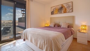 A bedroom with a bed, bedside lamps, a painting, and a view through a sliding door. - Vacation 'Casa Del Amanecer' with Sea View, Shared Pool and Wi-Fi (Lajares)