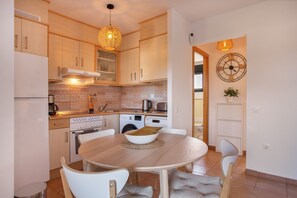 Una cocina moderna con armarios de madera, una mesa de comedor con sillas, una lámpara colgante y un reloj de pared.
