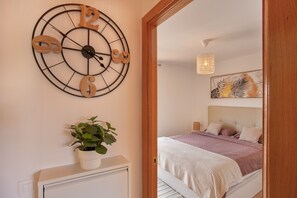 Un dormitorio con una cama, un reloj de pared, una planta en maceta y una puerta que da a otra habitación.