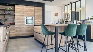 A modern kitchen with wooden cabinets, a built-in oven, and a bar area with green bar stools. - Cozy home in Valaurie (Valaurie)