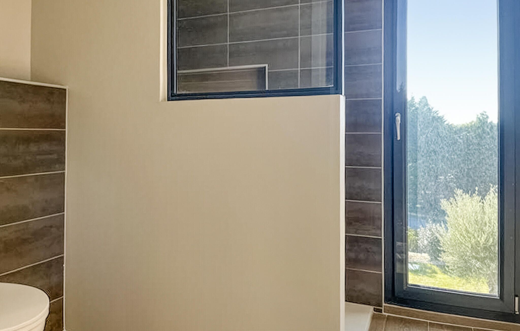 Een badkamer met een witte muur, een raam met uitzicht op groen en een deur met een hendel.