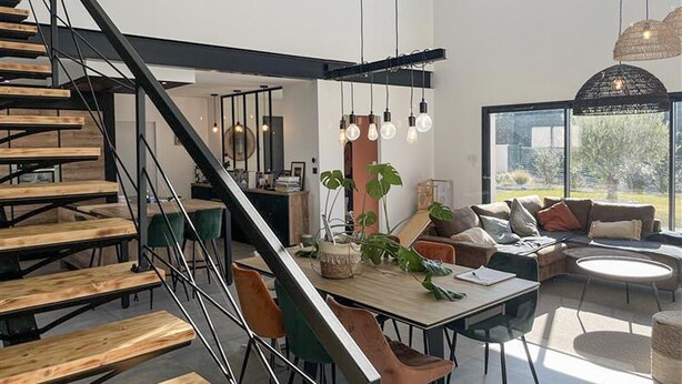 A modern interior with a staircase, dining area, and seating by a large window. - Cozy home in Valaurie (Valaurie)