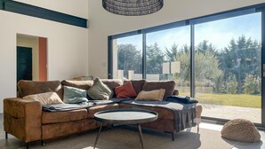 A modern living room with a large window, a brown sofa, and a round coffee table. - Cozy home in Valaurie (Valaurie)