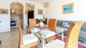 A modern living room with a glass dining table, wicker chairs, a grey sofa, and a kitchen in the background. - Apartment 'Charlie Beach' with Sea View, Balcony and Air Conditioning (castelsardo)