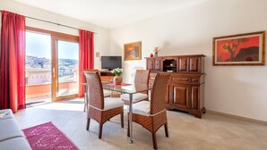 A living room with a glass table, wicker chairs, a TV, and a view through a sliding door. - Apartment 'Charlie Beach' with Sea View, Balcony and Air Conditioning (castelsardo)