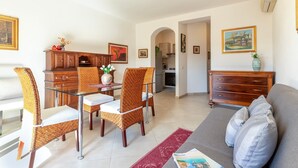 A living room with a sofa, dining table, chairs, and a kitchen area in the background. - Apartment 'Charlie Beach' with Sea View, Balcony and Air Conditioning (castelsardo)