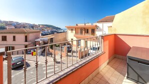 A balcony with a view of a street and buildings, a car parked on the street, and a trash bin. - Apartment 'Charlie Beach' with Sea View, Balcony and Air Conditioning (castelsardo)