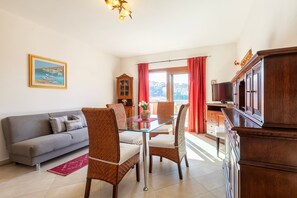 Un'area pranzo con tavolo in vetro, sedie in vimini, un divano grigio, un mobile in legno e un quadro appeso al muro.
