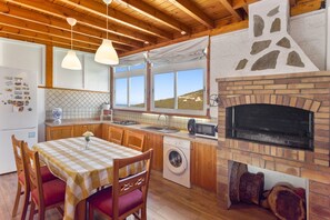 Una cocina con chimenea de piedra, armarios de madera, lavadora y una mesa con sillas.