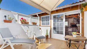 Patio esterno con tavolo e sedie, una poltrona reclinabile imbottita e vasi di piante.