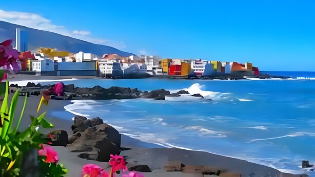 Un paese costiero con edifici lungo la riva, un cielo azzurro limpido e onde che si infrangono sulla spiaggia.