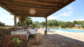 Un área de estar techada al aire libre con una piscina al fondo.
