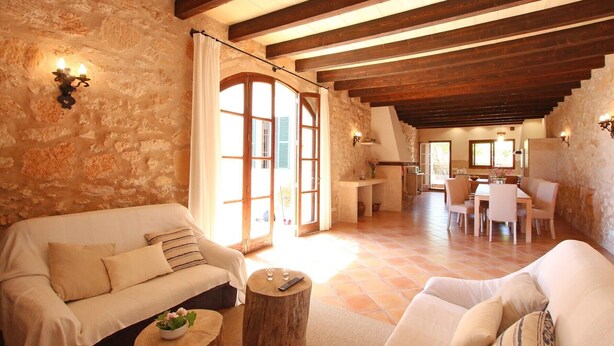 Un interior rústico con paredes de piedra, vigas de madera, un sofá, una mesa de comedor y una zona de cocina.