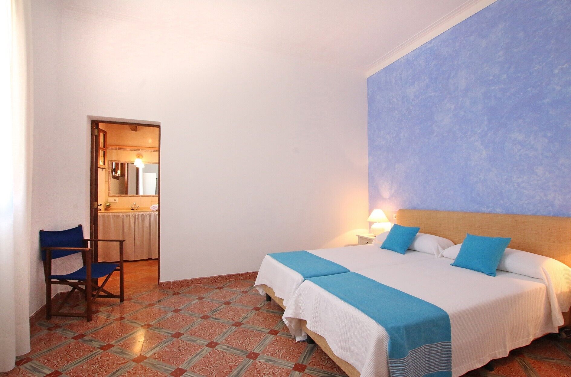 Ein Hotelzimmer mit einem Bett, Nachttischlampen, einem Sessel und einem durch eine offene Tür einsehbaren Badezimmer.