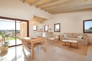 A spacious living area with a dining table, sofa, and chairs, large windows, and a view of the outdoors.