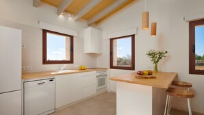 A modern kitchen with white cabinetry, a wooden countertop, a built-in dishwasher, a stove, and a bar stool. - Rural House 'Son Rossinyol Nou - Ses Figueretes' with Mountain Views, Private Pool and Wi-Fi (Illes Balears)
