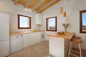 Une cuisine moderne avec des meubles blancs, un plan de travail en bois, un lave-vaisselle encastré, une cuisinière et un tabouret de bar.