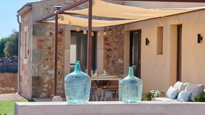 A stone building with a patio area, two large bottles, a table, and a sofa. - Rural House 'Son Rossinyol Nou - Ses Figueretes' with Mountain Views, Private Pool and Wi-Fi (Illes Balears)
