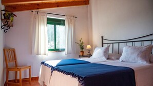 A bedroom with a bed, a chair, a window with curtains, and a lamp on a nightstand. - Apartment 'Casa Rural Maximón Azul' with Sea Views, Wi-Fi and Air Conditioning (Los Caños de Meca)