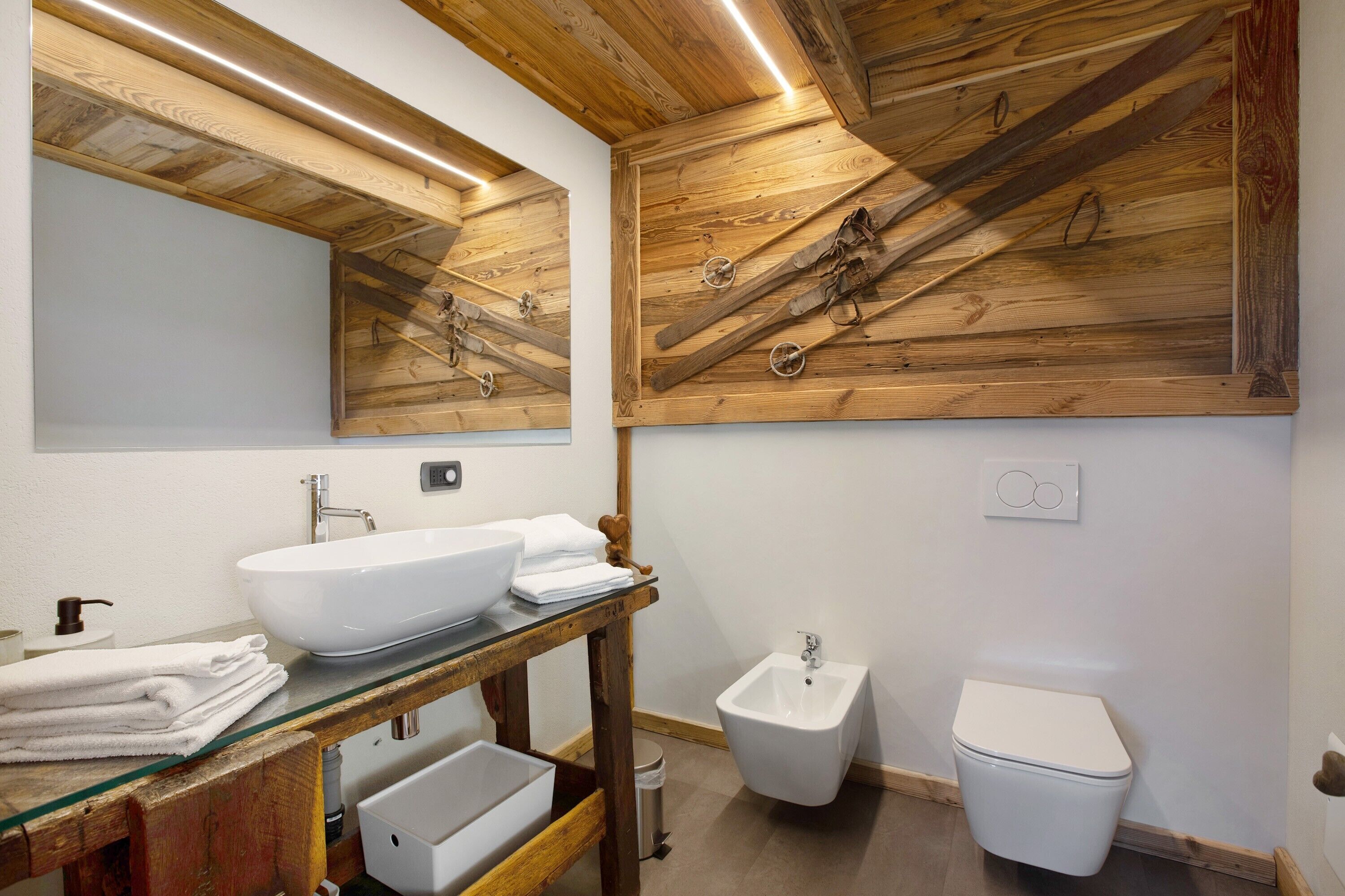 Un bagno con soffitto in legno, lavabo in vetro, bidet e water.
